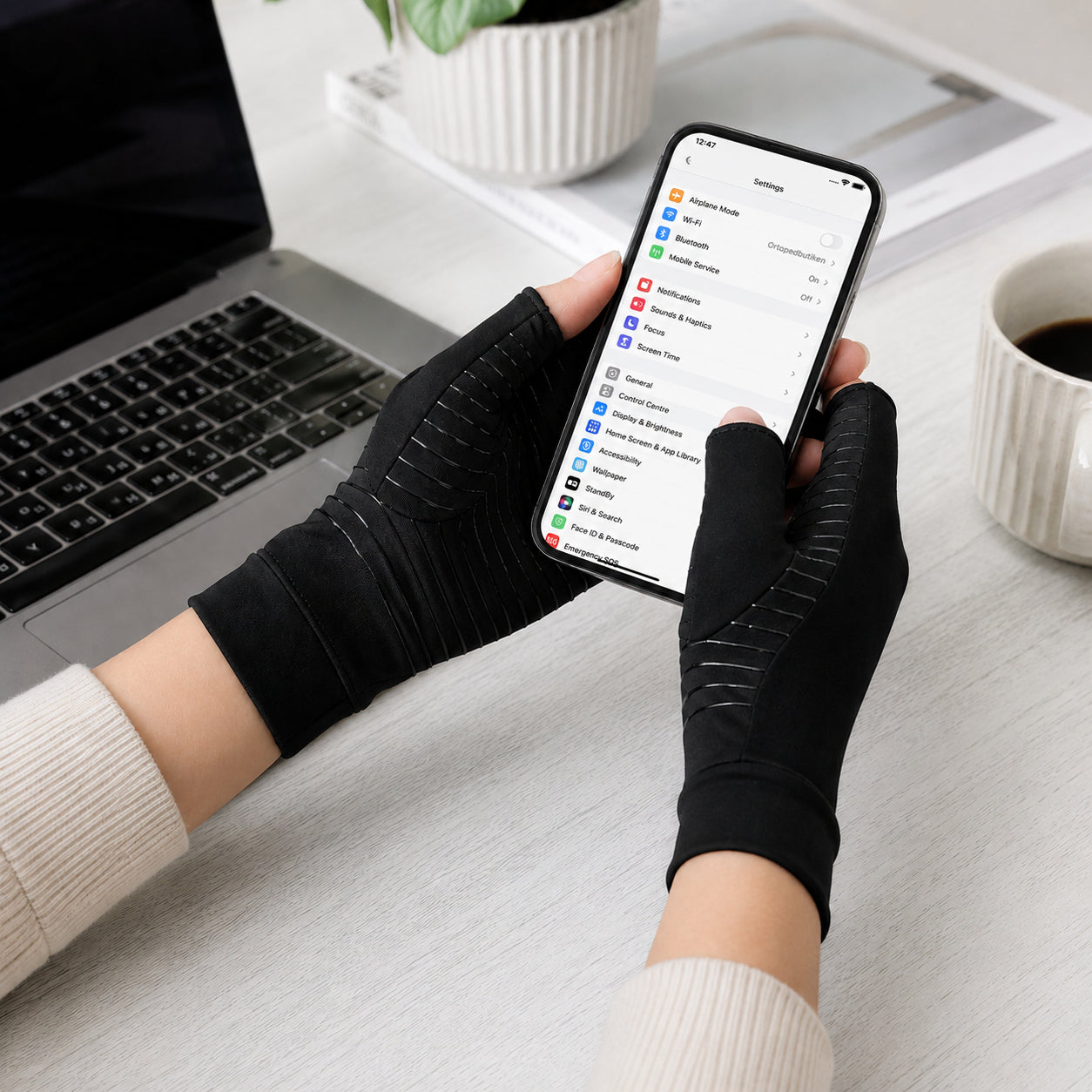 Une personne utilise des gants de compression en cuivre noirs en utilisant son téléphone.