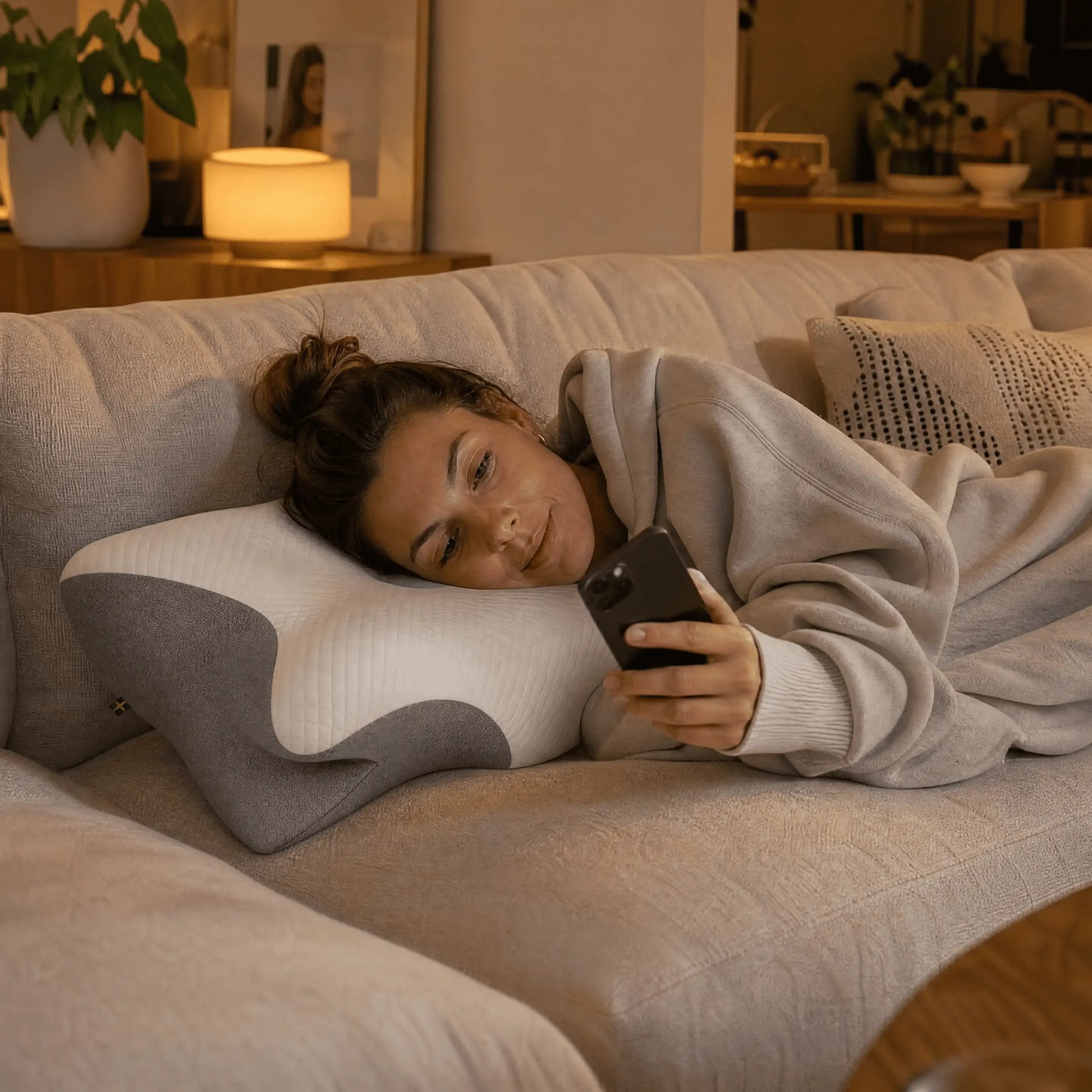 Kvinna som vilar på ergonomisk sovkudde i soffan och använder mobiltelefon hemma